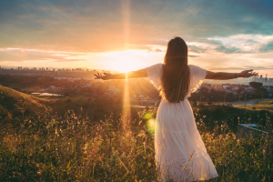 woman wearing white dress facing the golden hour in the mountains